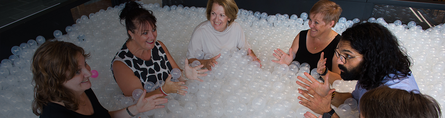 Group of happy middle aged people in a pit of plastic balls discussing something