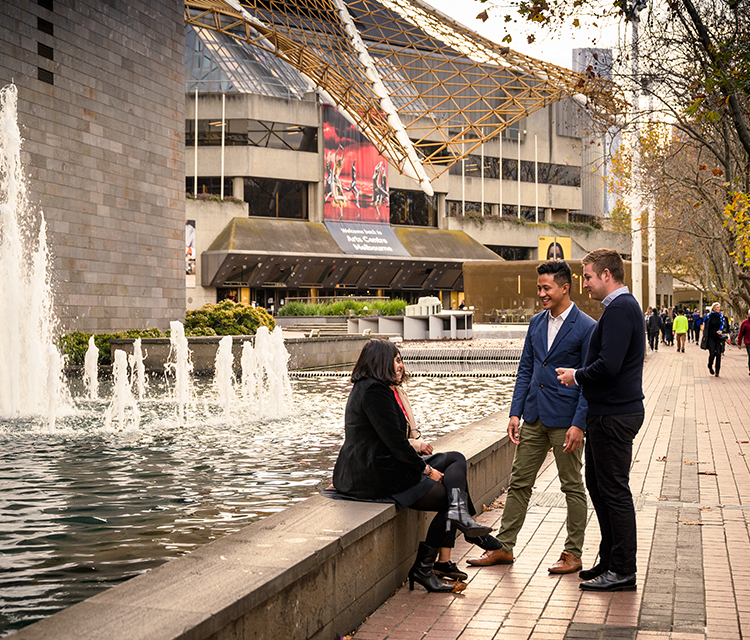 Happy group of people conversing outside Melbourne NGV with the Arts Centre in the background