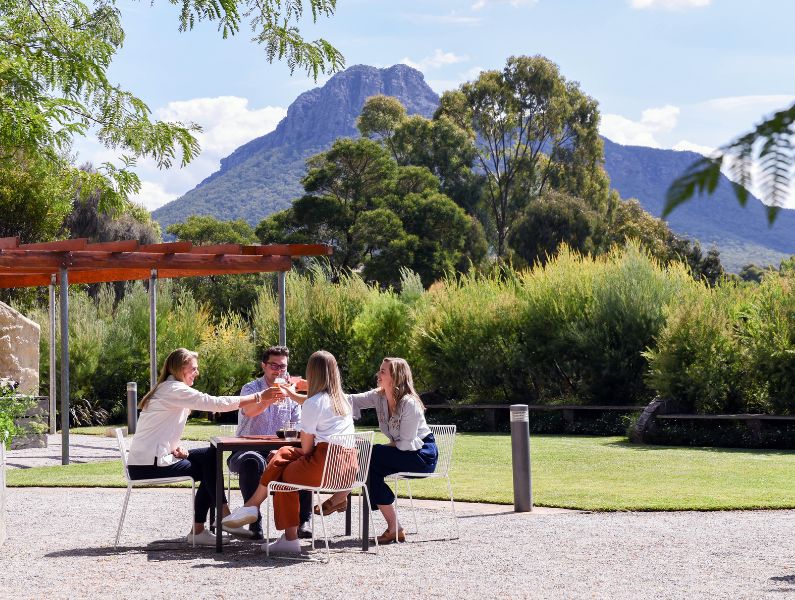 Grampians in the background, trees and people at a table having a drink in the foreground