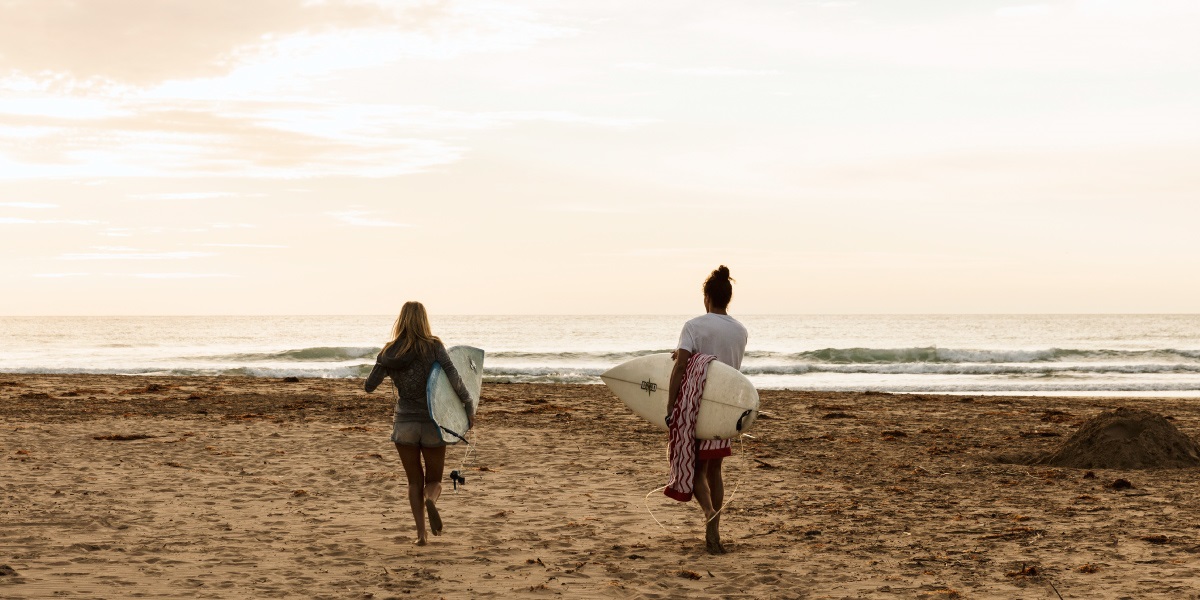 two people holding their surfboards as they walk towards the sea.